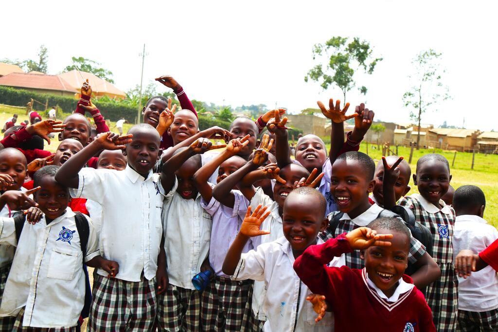 A large group of primary school pupils in uniform waving and smiling outside their school